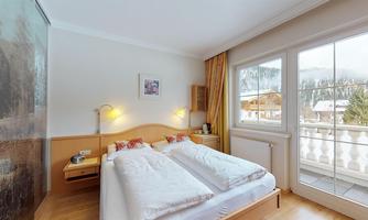 A cozy bedroom with two single beds and light wood decor. Large windows offer a view of the surrounding landscape.