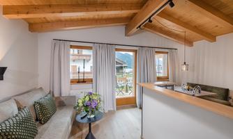 A cozy living space with a wooden beam ceiling and large windows. Stylish furniture and a blooming vase give the room an inviting atmosphere.