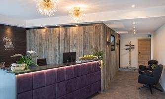 A modern reception hall with wooden paneling and elegant lighting. The reception desk is in purple and decorated with plants.