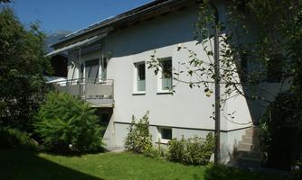 A modern house with a well-maintained garden. The facade is bright and the surroundings are green and inviting.