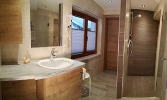 A modern bathroom with bright tiles and a rain shower. The wash area features an elegant sink arrangement and large windows for natural light.