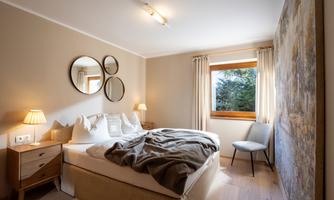 A modern bedroom with a cozy bed and soft lighting. Large windows offer a view of nature outside.