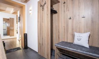 A stylish entrance area with wooden furniture and a bench. Several coat hooks are hanging on the wall, and a mirror is visible in the background.