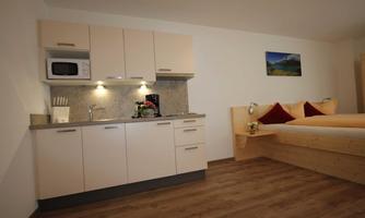 A cozy apartment with a small kitchenette and a bed. The bright walls and wooden floor create an inviting atmosphere.