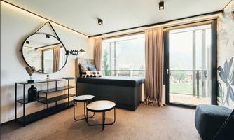 A modern living room with large windows and a view of nature. The decor is stylish, featuring a round mirror and minimalist tables.