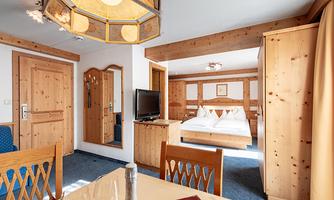 A cozy hotel room with wooden furniture and a large window. The room features a dining table, a television, and a comfortable bed.