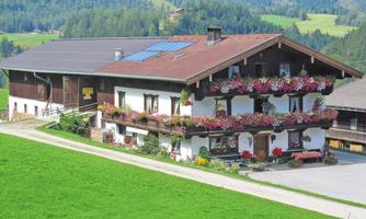 A traditional farmhouse with flower boxes and a green lawn. In the background, gentle hills and forests can be seen.