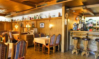 A cozy restaurant with wooden walls and warm lighting. There are tables with colorful chairs and a well-equipped bar.