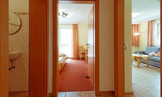 A bright hallway with doors to different rooms. On the right side, a living room can be seen with a sofa and a table.