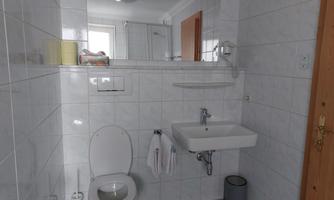 A simple bathroom with white tiles. It contains a toilet, a sink, and a mirror.