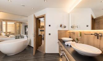 A modern bathroom with a freestanding bathtub and two sinks. The wooden elements and the elegant design create a cozy atmosphere.