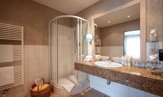A modern bathroom with a shower cabin and a large mirror. The sink area is made of beautiful granite with toiletries on the shelf.