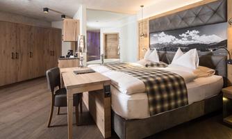 A modern hotel room with a large bed and a wooden table. The decor is cozy and offers a view of the adjacent landscape.