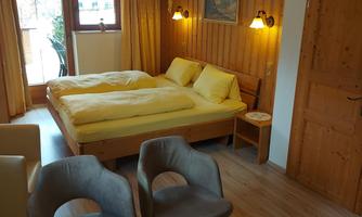 A cozy bedroom with a double bed and yellow bedspreads. The room has wooden walls and a small seating area with two chairs.