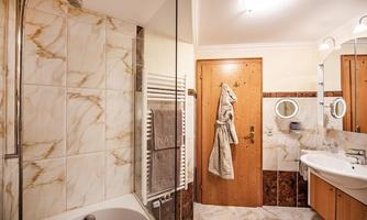 A modern bathroom with marble tiles and a bathtub. The furnishings include a mirror, towels, and a wooden cabinet.