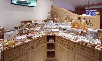 A rich breakfast buffet with a variety of dishes and drinks. Fresh fruits, cakes, and juices are beautifully arranged on a wooden shelf.