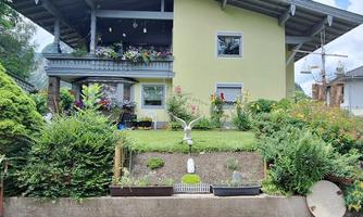 A modern house with a large balcony and colorful flowers in the garden. The surroundings are well-kept and inviting.