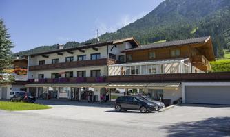 A modern building in the mountains with several floors. There are parked cars and green meadows in the background.