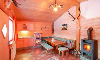 A cozy room with wooden paneling, a fireplace, and a small kitchen. There is a sitting area with a table and benches as well as decorative details on the walls.