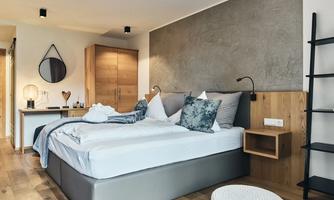 A modern bedroom with a large bed and decorative pillows. The walls are in neutral colors and there is wooden furniture.