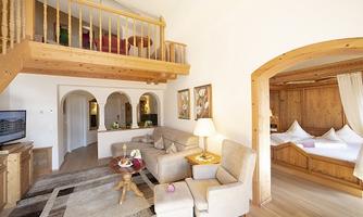 A cozy living space with wooden details and a sleeping area in the background. The decor is bright and inviting, with an upper floor and modern furniture.