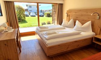 A cozy room with a double bed and wooden furniture. Large windows offer a view of the garden.