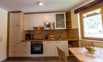 A modern kitchen with wooden tiles and white cabinets. The table is next to a window with a view outside.