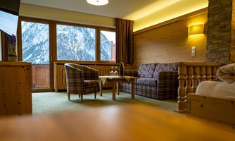 A cozy hotel room with two armchairs and a table. A mountain landscape can be seen through the large windows.