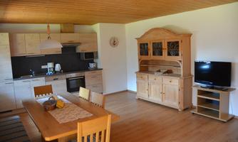 A bright and cozy kitchen with a dining table. In the background, there is a wooden cupboard and a television.