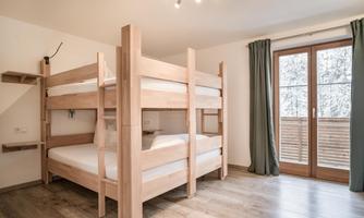 A modern bedroom with a wooden loft bed. Large windows let in plenty of light and offer a view of the outdoors.