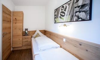 A simple room with a single bed and light wooden details. A modern artwork hangs on the wall, and a wardrobe is next to the bed.