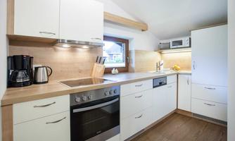 A modern kitchen with white cabinets and wood details. The equipment includes a coffee machine, a refrigerator, and an oven.