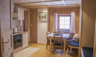 A cozy kitchen and dining area with wood paneling. There is a bright window front and a table with chairs.