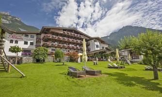 A cozy hotel with balconies, surrounded by green meadows and mountains. The sky is clear, and the landscape invites you to relax.