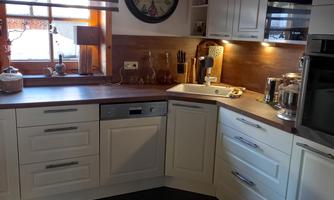 A modern kitchen with white cabinets and a wooden floor. Sunlight falls through the window and illuminates the countertop.