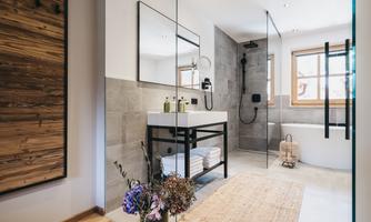 A modern bathroom with a glass shower and an elegant sink. The warm wooden elements and fresh flowers create an inviting atmosphere.