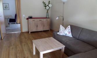 A cozy living room with a gray sofa and a wooden table. The room has a warm wooden floor and a bright color scheme.
