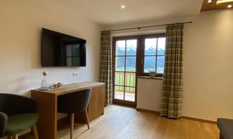 A comfortable room with a television, table, and two chairs. Large windows offer a view of the mountains.