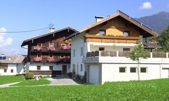 A charming house in Alpine style with wooden cladding and blooming balconies. The green meadow and mountain backdrop give the surroundings an idyllic atmosphere.