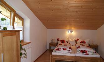A cozy bedroom with two beds and red floral bedding. A wooden ceiling and a window create a bright, inviting atmosphere.