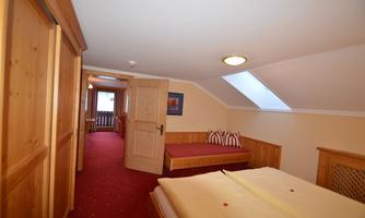 A cozy room with wooden paneling, a double bed, and a single bed. The room has a window facing the hallway and a warm, inviting atmosphere.