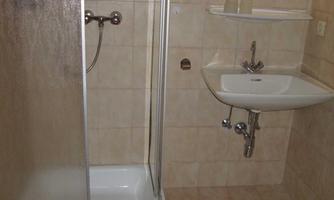 A small bathroom with a shower, sink, and bright tile design. The walls are beige, and the fixtures are simple and functional.