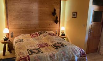 A cozy bedroom with a large bed and a colorful duvet. The walls are made of wood, and there is soft lighting on both sides of the bed.
