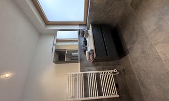 A modern bathroom with an elegant vanity and a large mirror. A radiator is mounted on the wall, and a window lets in natural light.
