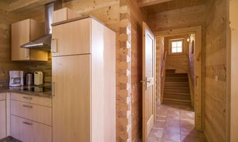 A cozy wooden kitchen with modern appliances and a staircase that leads to the upper rooms. The space has natural wooden walls and plenty of light.