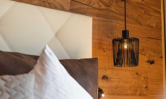 A modern bedroom with a white headboard and a stylish pendant light. The wooden wall gives the room a cozy atmosphere.