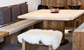 A modern dining room with a large wooden table and benches. On the table lies a decorative basket with some snacks.