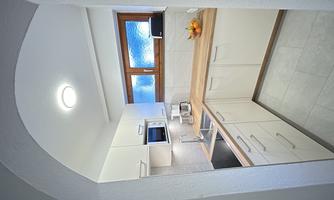 A modern kitchen with white cabinets and a wooden countertop. Natural light comes in through the window, and there is a fruit bowl on the countertop.