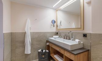 A modern bathroom with a large mirror and a wooden sink cabinet. The walls are light, and the floor is made of elegant stone.