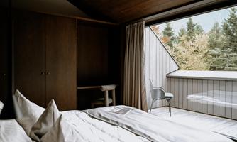 A modern bedroom with a large window that leads to a balcony overlooking greenery. The decor is simple and elegant, perfect for a cozy retreat.